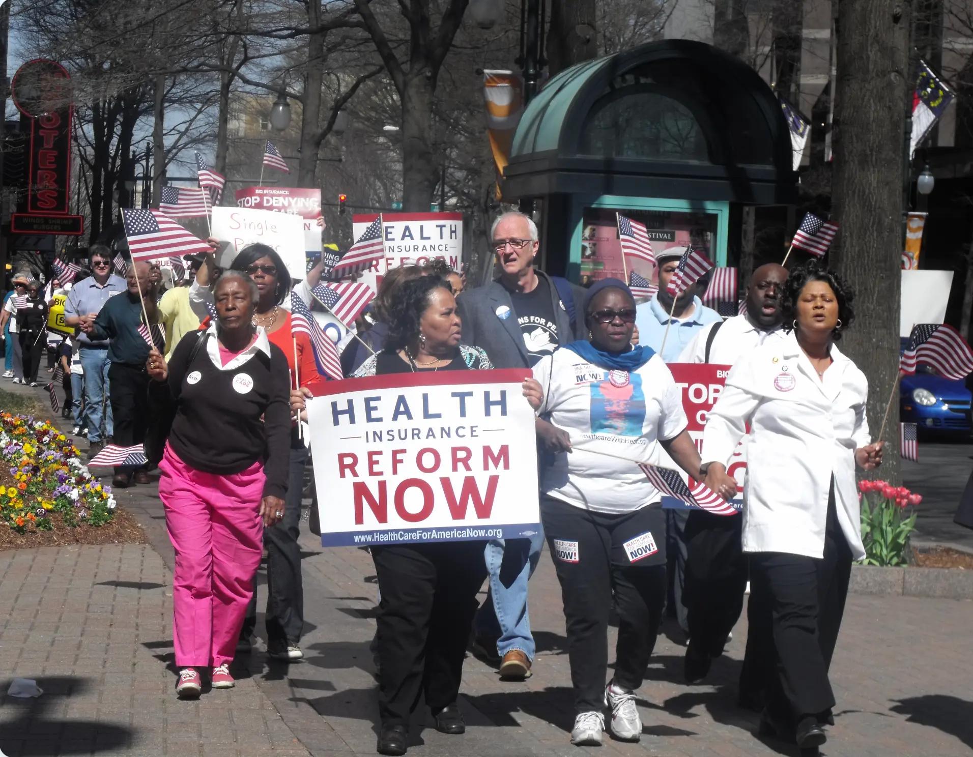 Marchers in uptown Charlotte carrying a large 'Health Insurance Reform Now' sign and American flags during the 2010 CHCC healthcare march.